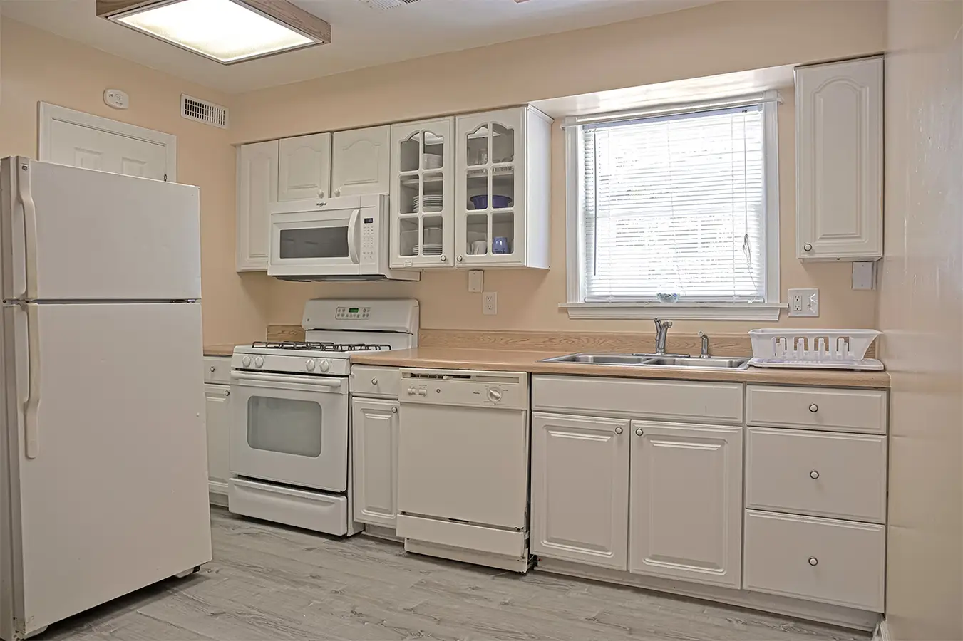 A white apartment kitchen with a full-size cooker, fridge, dishwasher and a window over the sink