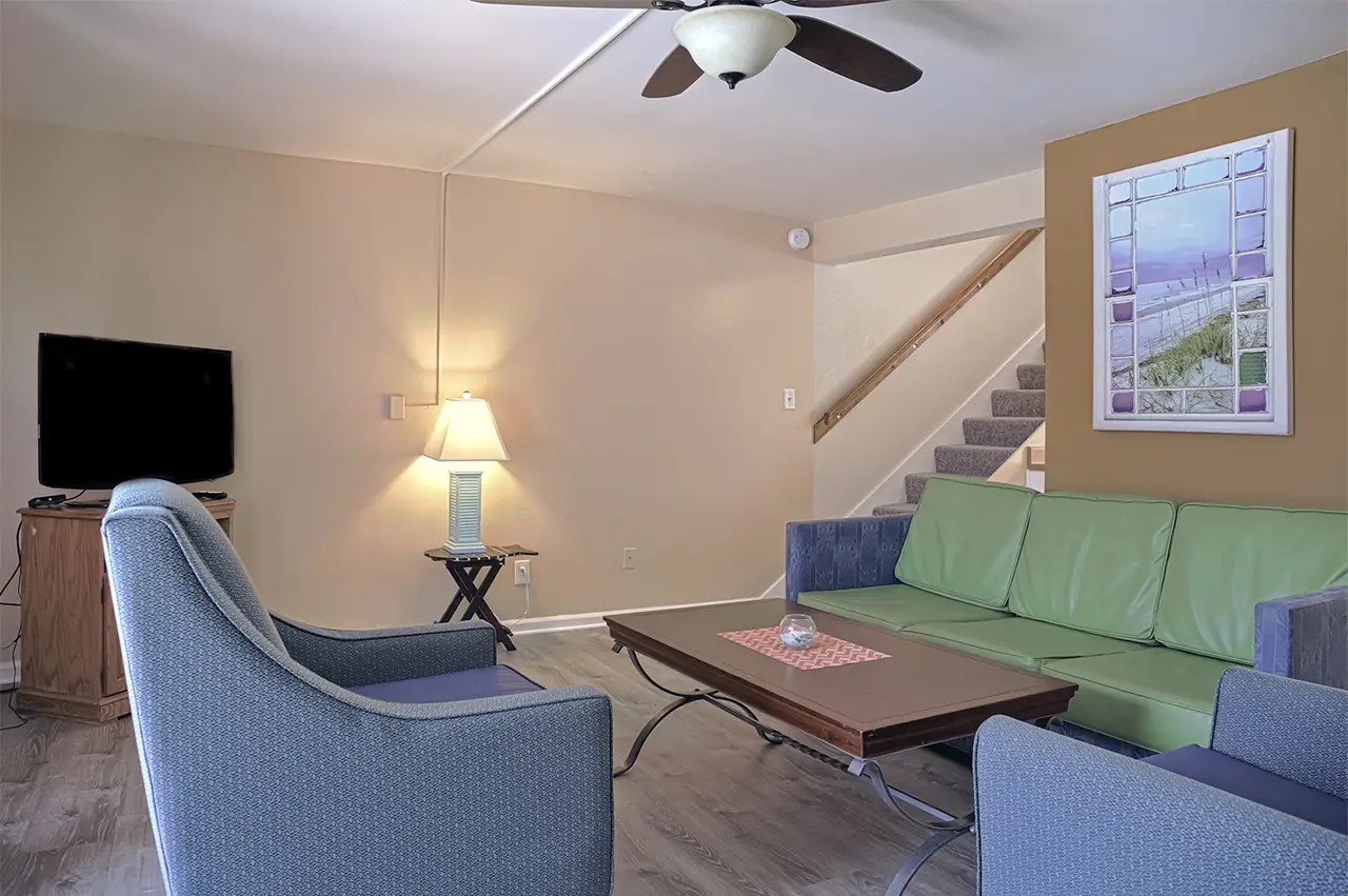 An apartment living room with a green sofa, armchairs and a staircase up to the bedrooms