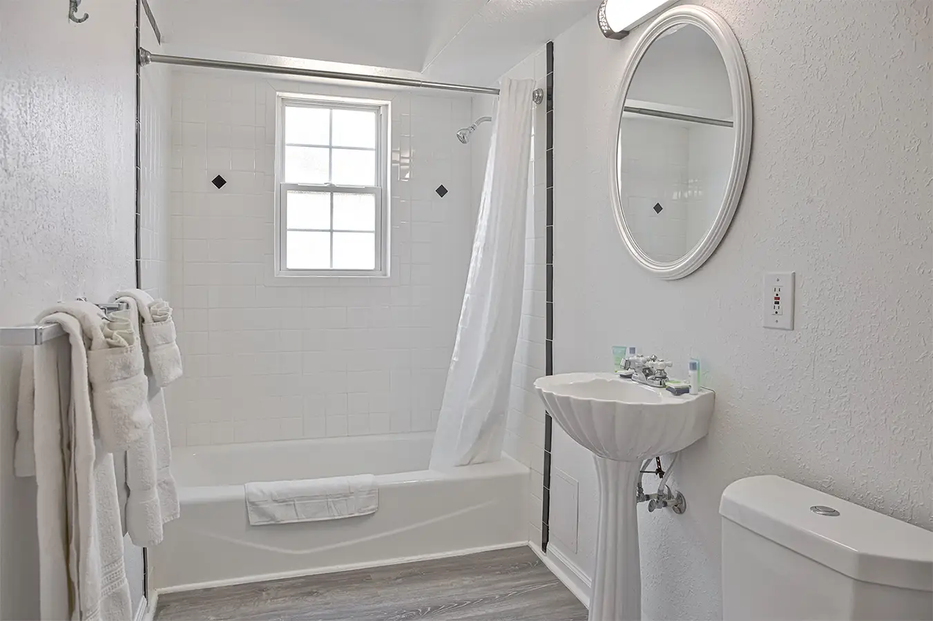 A white guest bathroom with a shower over the bath, a basin and an oval mirror