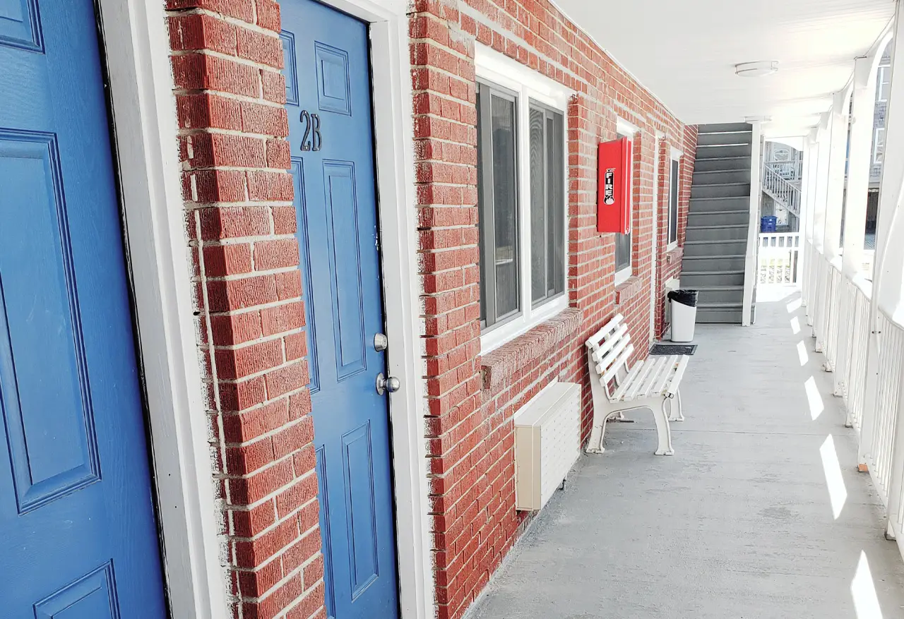 The red brick walkway along the front of the motel, with blue-painted room doors and a bench outside