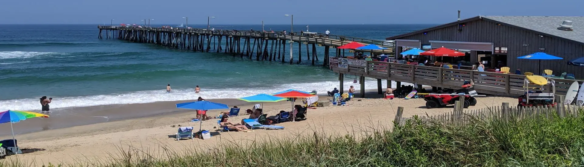 Nags Head Fishing Pier and the beach below it, with umbrellas along the sand