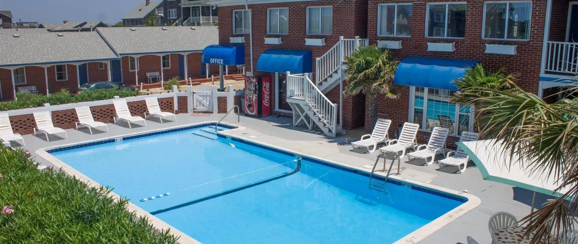 The outdoor pool in front of the red brick building, with blue awnings and sun loungers
