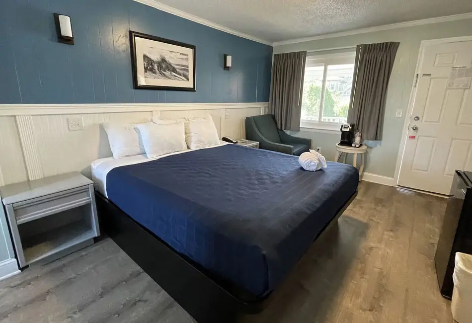 King bed with a navy cover and armchair in a Colonial Inn guest room
