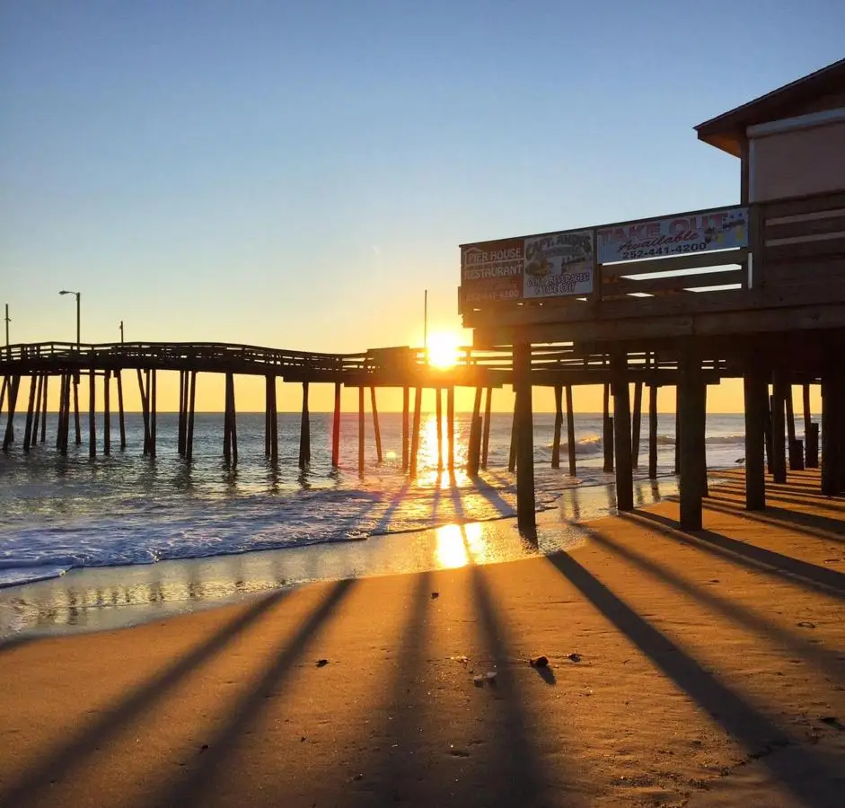 Sunrise seen through the pilings of the fishing pier, casting long shadows on the wet sand
